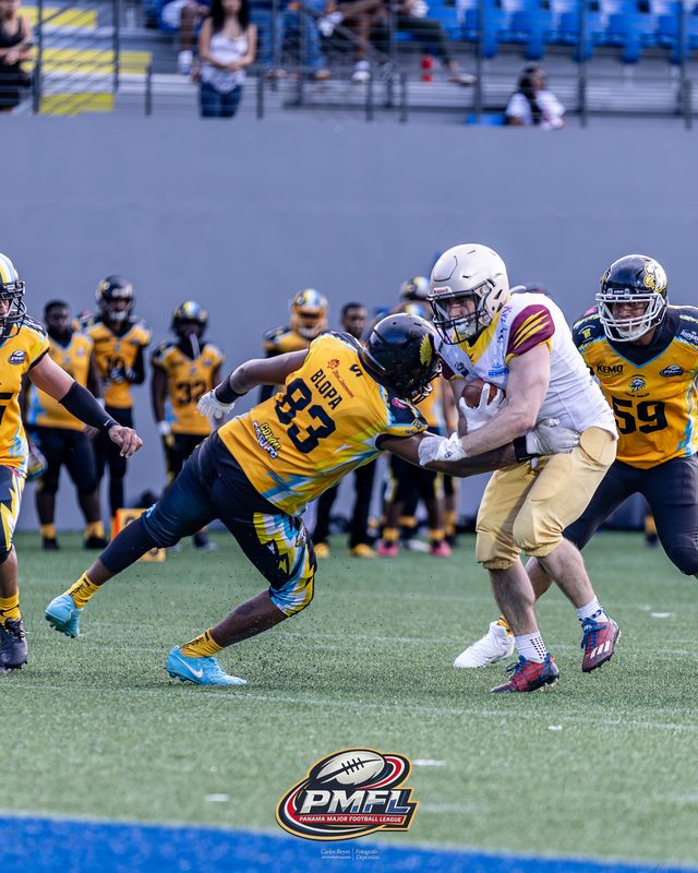 El número 83 de los Colón Eagles frena a un receptor rival cerca de la banda